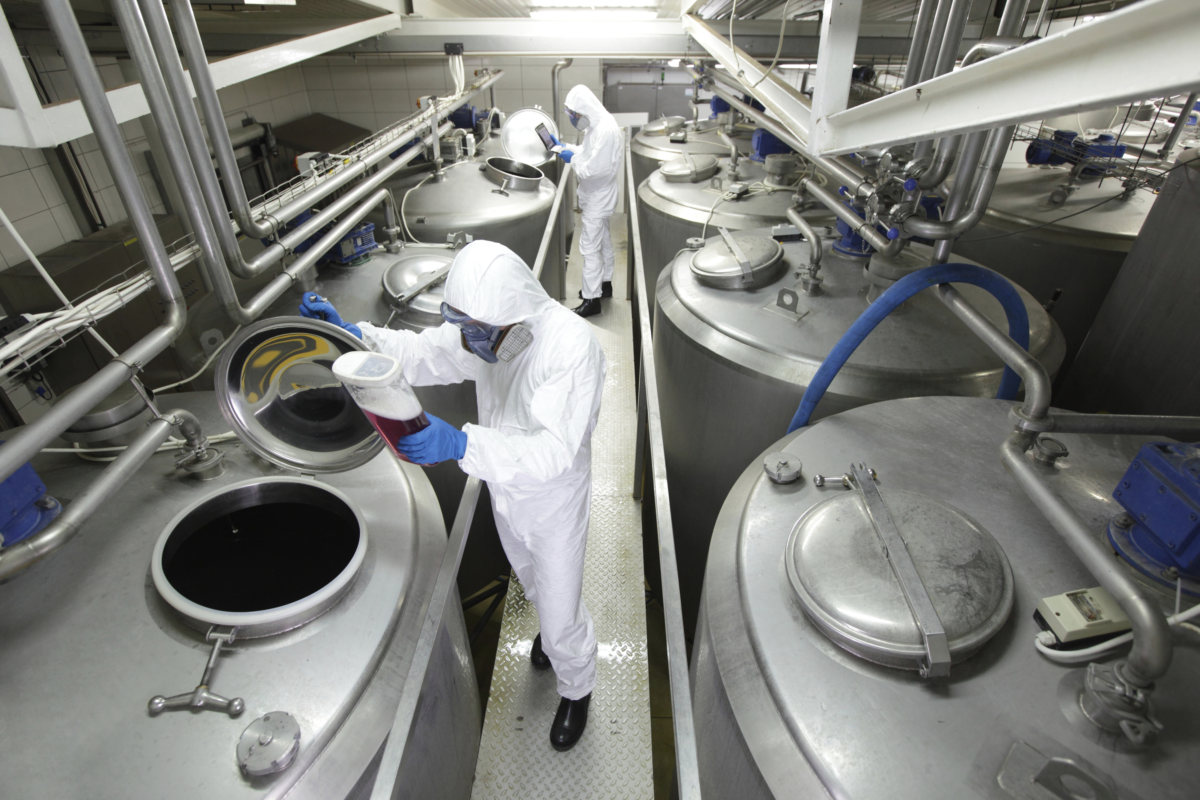 Two workers working with industrial process tanks in plant